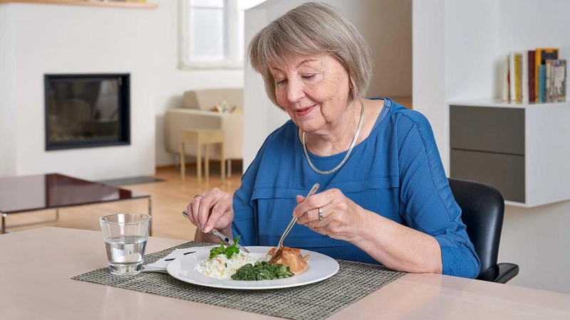Seniorin sitzt am Tisch und isst ihre Mahlzeit