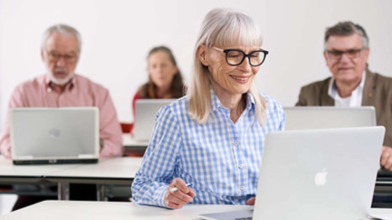 Eine ältere Frau mit Brille sitzt in ihrem Arbeitszimmer am Computer