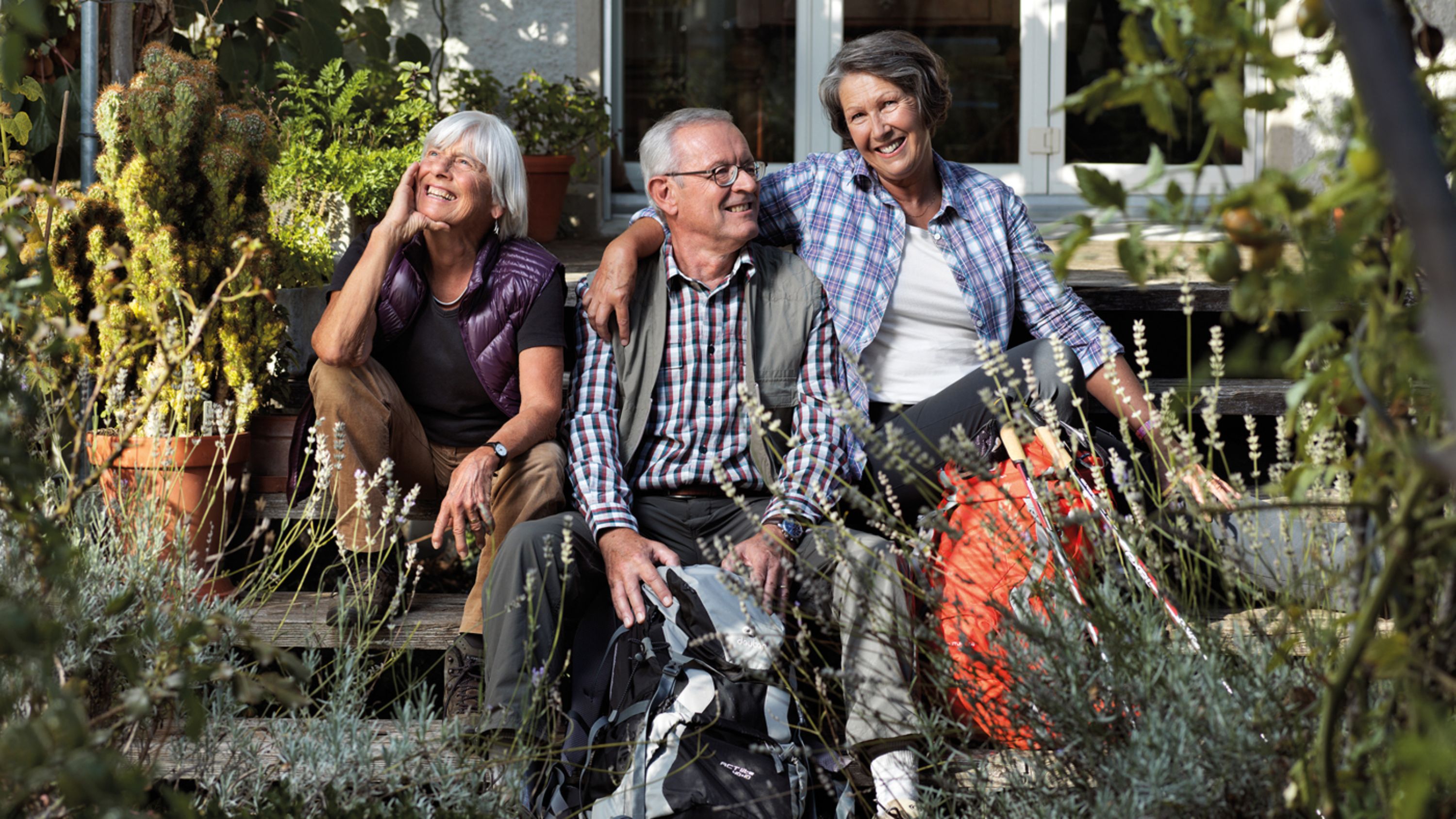 Drei Senioren sitzen auf der Treppe im Garten und lachen