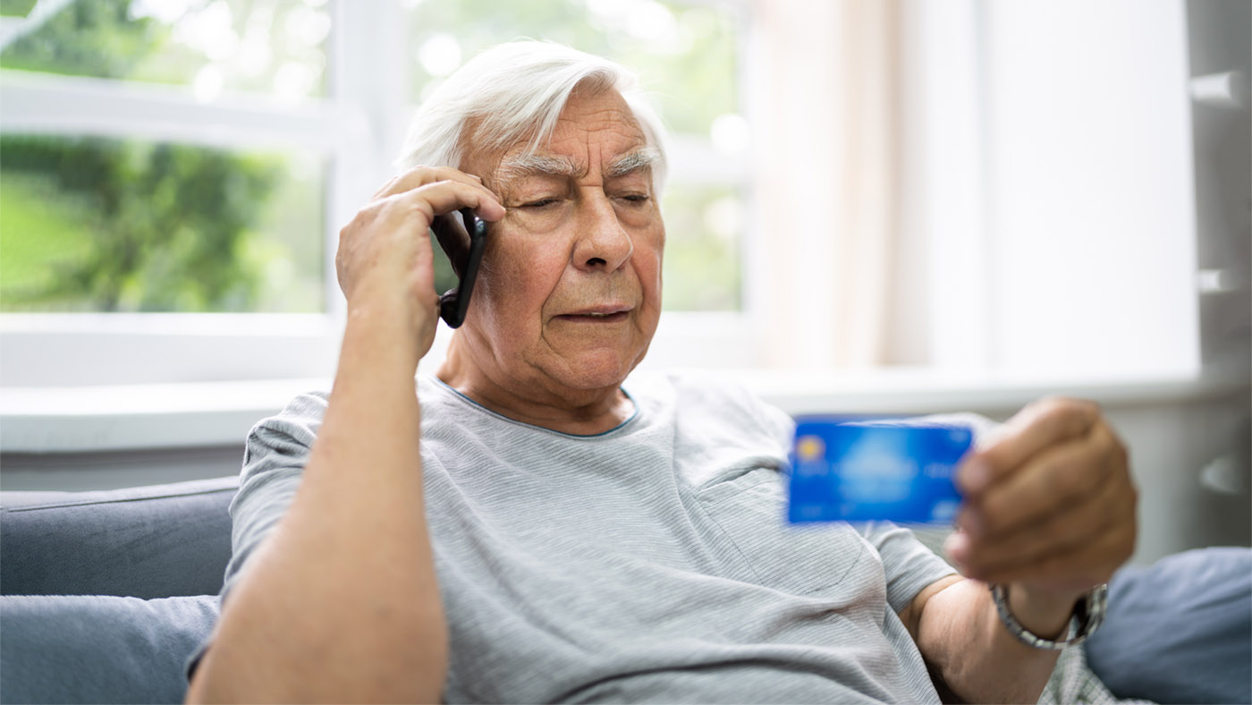 Ein Senior ist am Telefon und hält gleichzeitig eine Kreditkarte in der Hand
